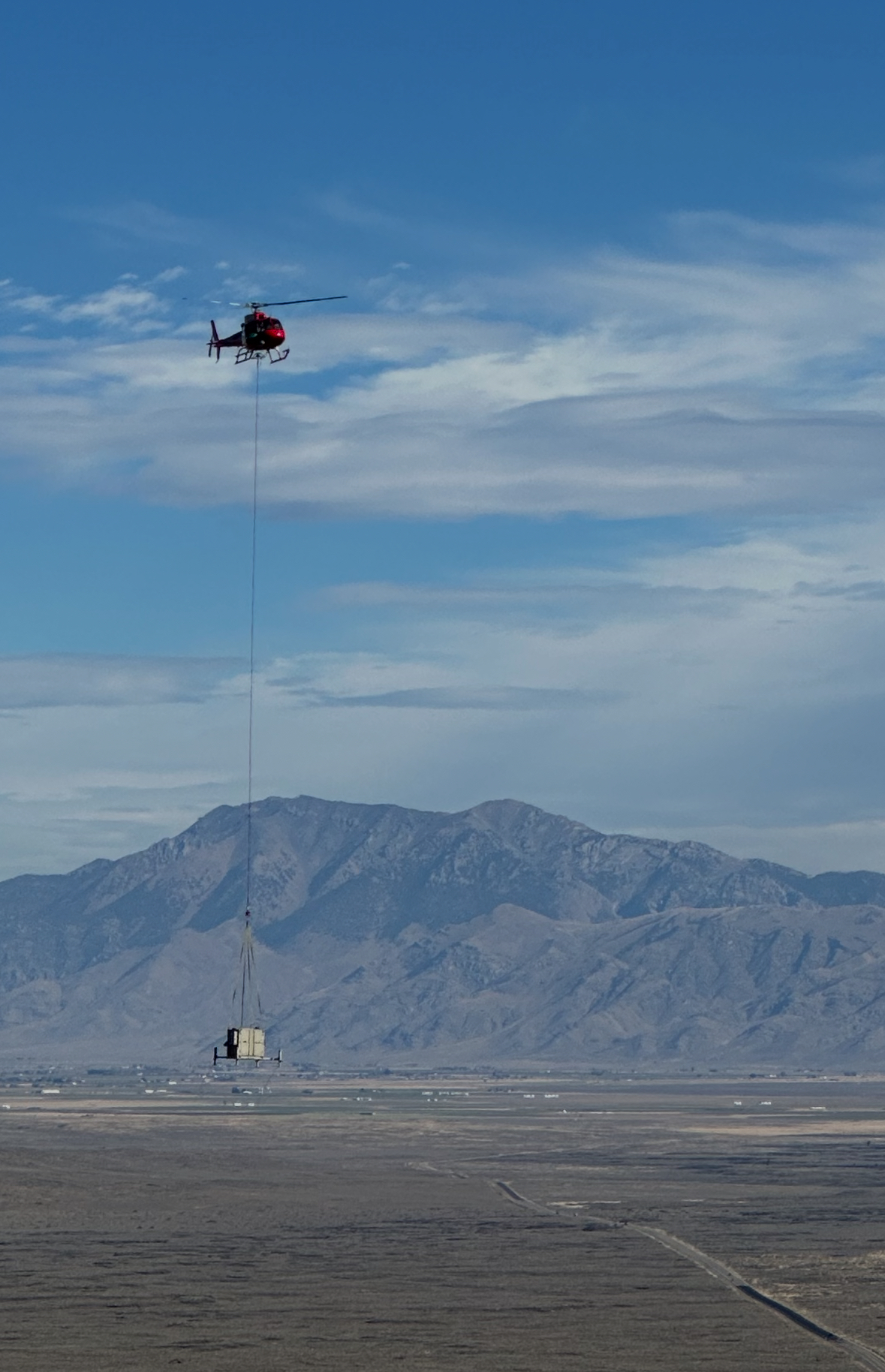 Helicopter sling-loading a communications shelter at a remote site